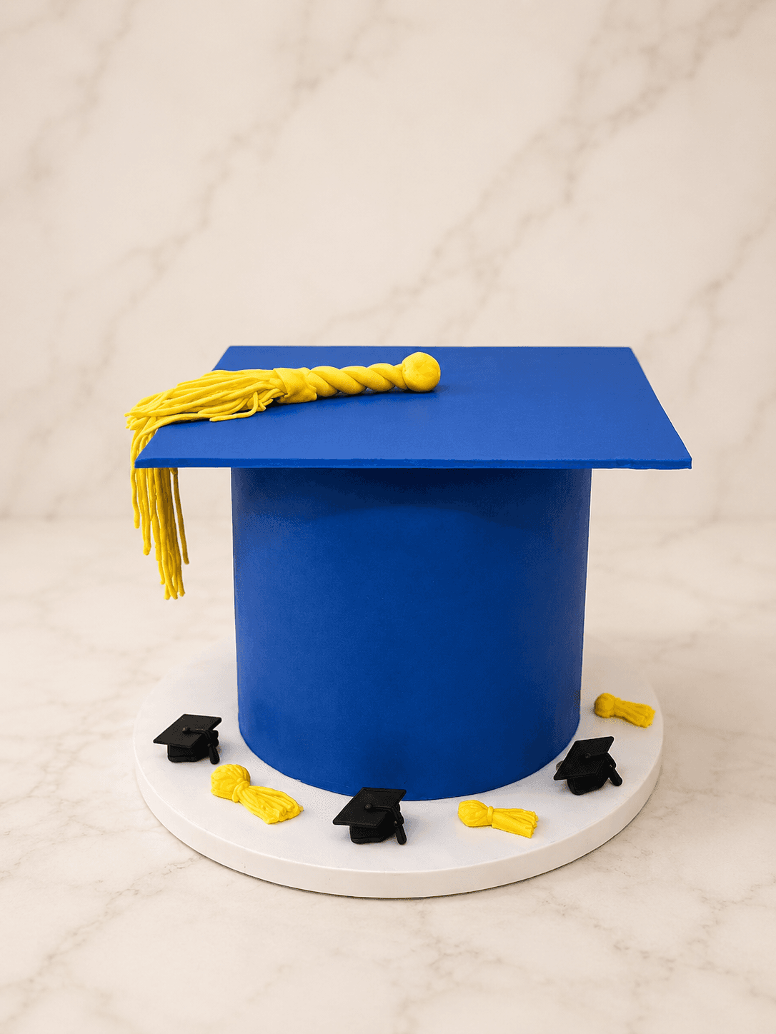 Royal blue graduation cap cake with a yellow fondant tassel and mini mortarboard toppers