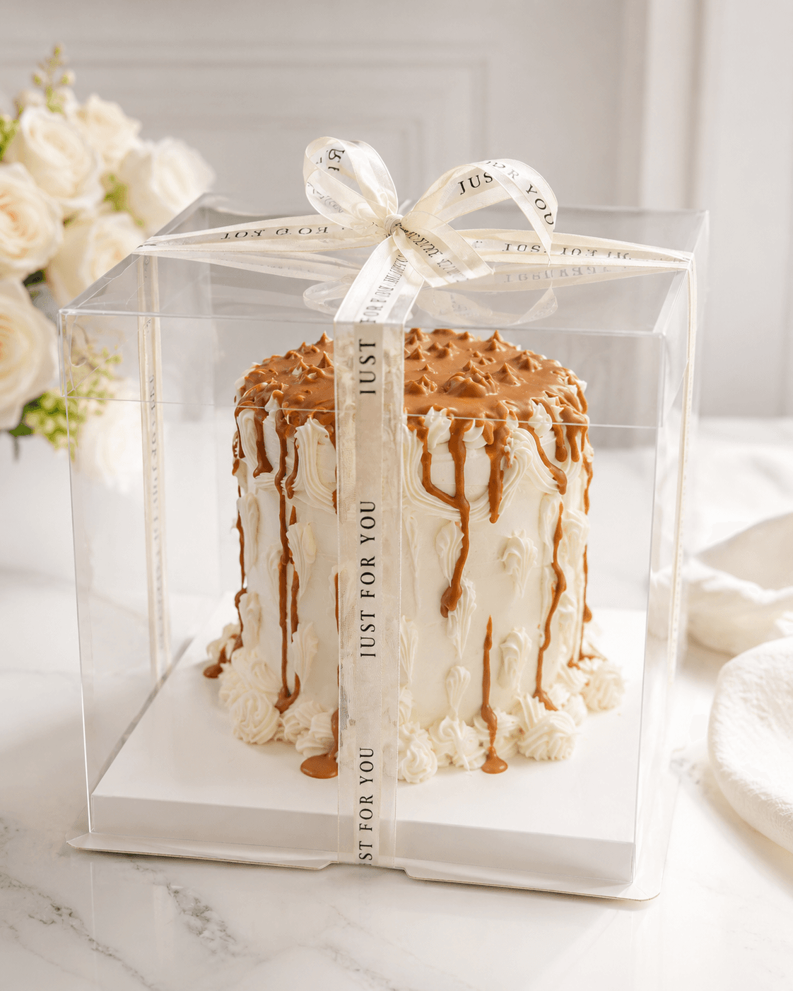 Tall buttercream cake with caramel drip and a Just For You ribbon