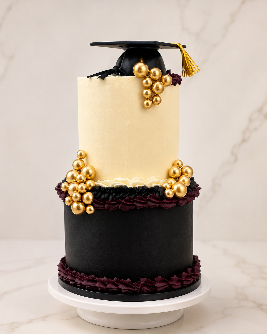 Two-tier black, white, and gold graduation cake with gold beads and a cap topper