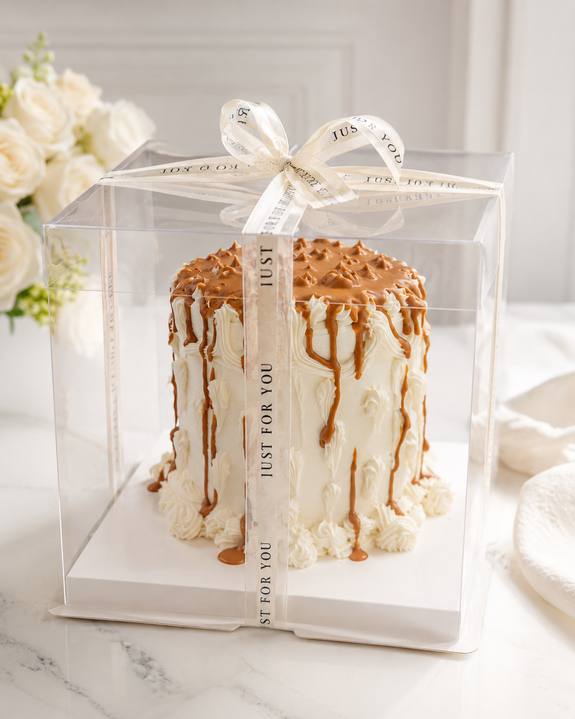 Tall buttercream cake with caramel drip and a Just For You ribbon